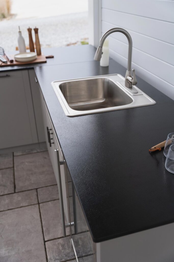 Stainless drop-in sink with a pull-down faucet set into a black countertop on gray Agora outdoor cabinets.