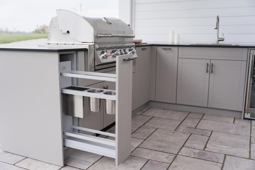 Light gray Agora cabinet with a narrow vertical pull-out caddy holding stainless utensil cups below a built-in Blaze grill.