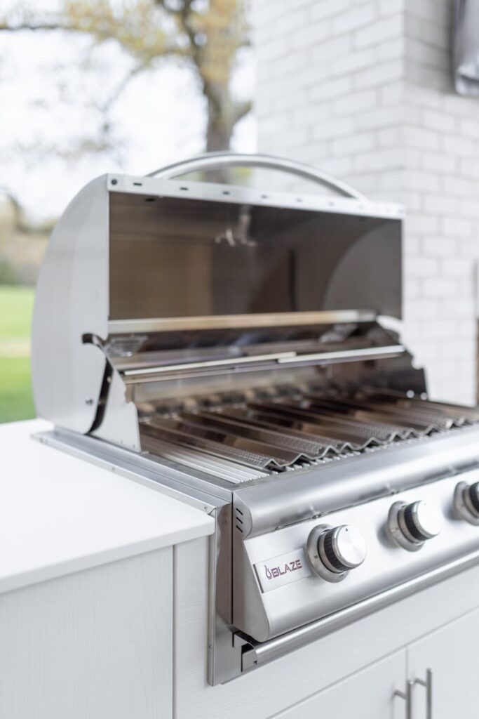 Blaze four-burner built-in gas grill with hood open inside a white Agora outdoor cabinet against a white brick wall.