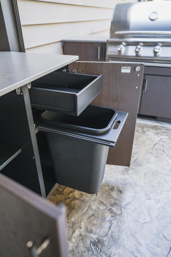 Espresso Agora outdoor cabinet with its pull-out trash drawer and black bin extended, branded Agora logo on the door.