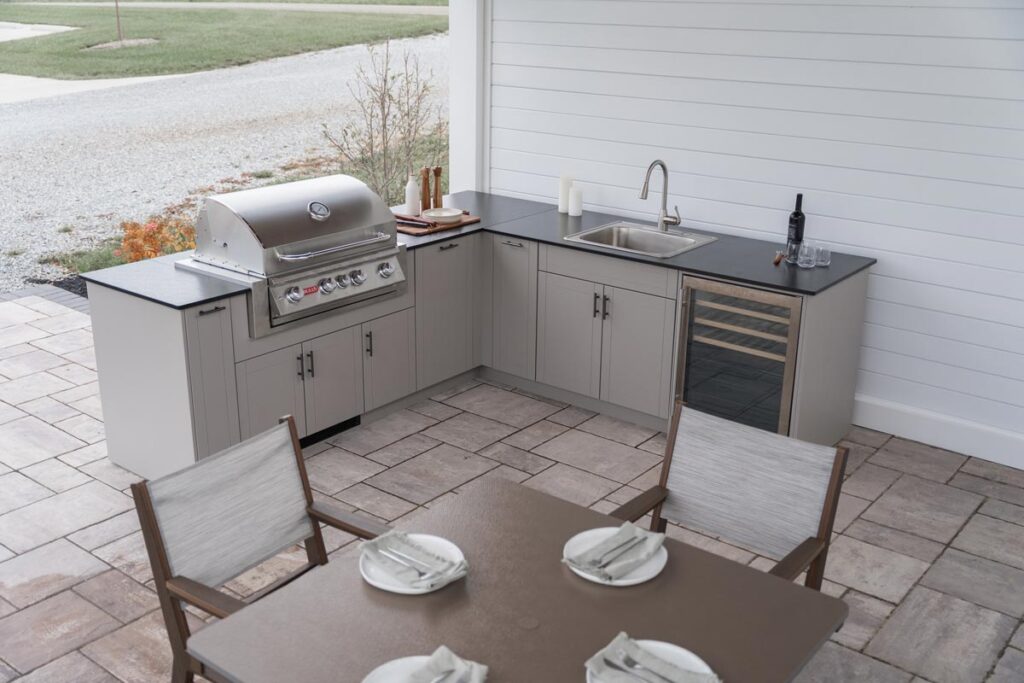 Overhead view of an L-shaped gray Agora outdoor kitchen with a Blaze grill, sink, wine fridge, and set dining table.